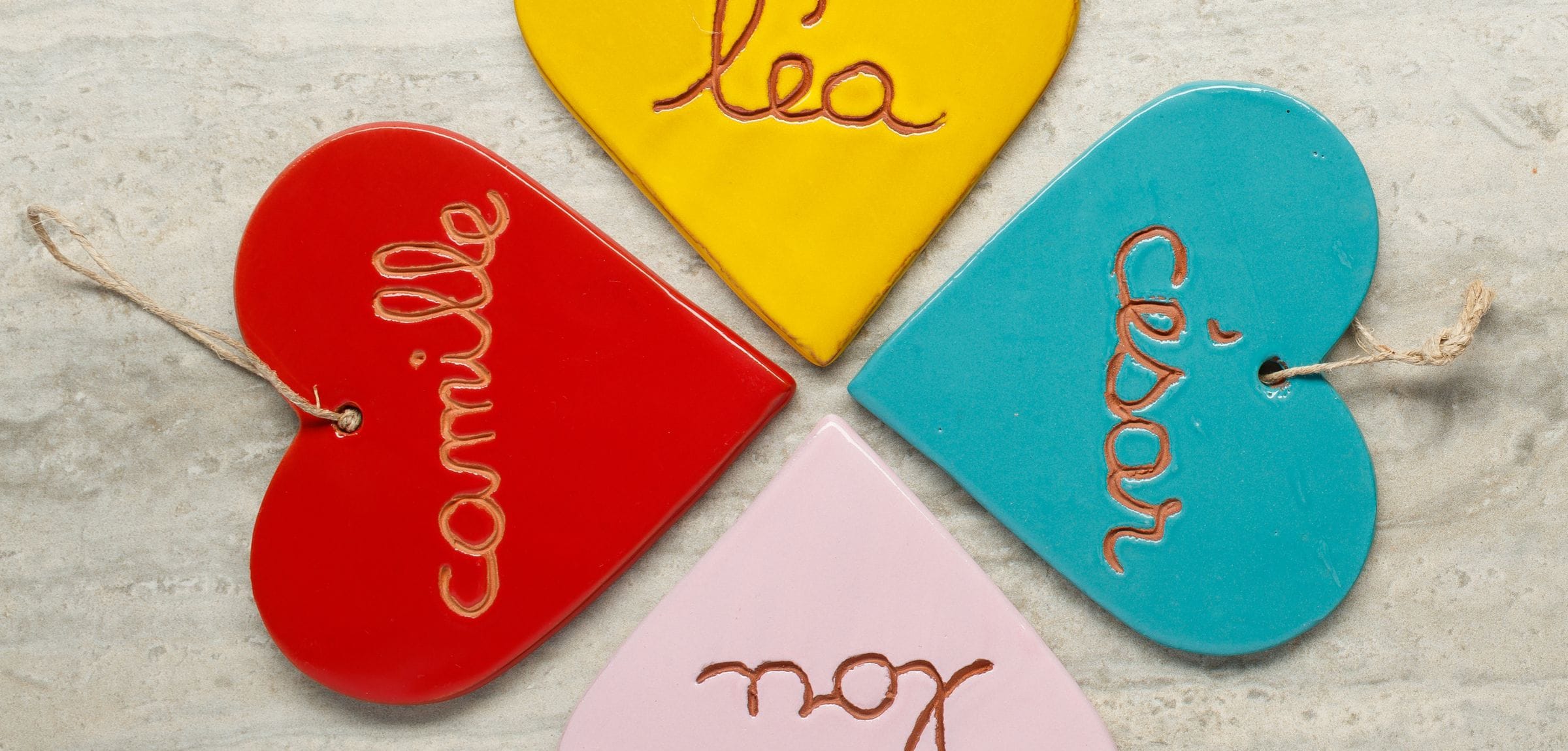 Quatre cœurs en faïence émaillée, gravés aux prénoms camille, léa, césar et lou, disposés en rosace sur une pierre claire